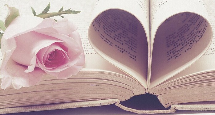 an old book with a pink rose sitting on it and the middle pages flipped into a heart for a valentine