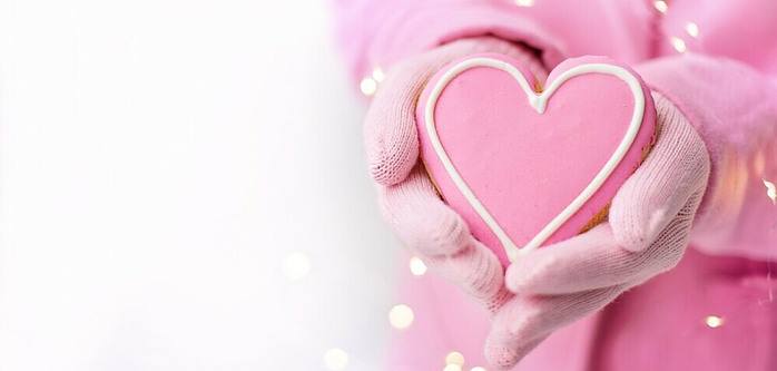 young hands holding a pink heart in the snow